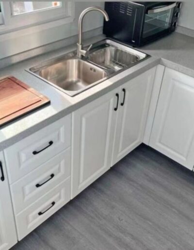 Prefabricated kitchen unit featuring white cabinetry, stainless steel sink, and compact, efficient design.