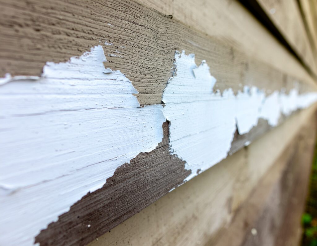 Close-up of severely peeling white paint on weathered wooden exterior siding, indicating the need for professional exterior renovation or repainting services.