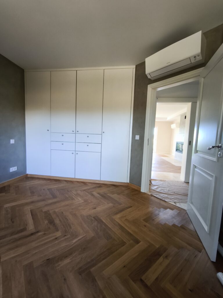 Renovated bedroom at Quinta Girassol featuring herringbone oak flooring, Kalklitir lime paint walls in sage grey, and custom floor-to-ceiling built-in wardrobes — luxury villa renovation by Build It Now, Algarve
