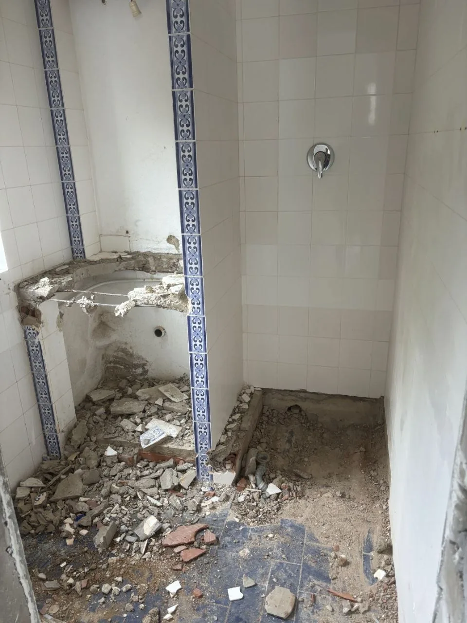 Bathroom during strip-out, with exposed services and blue floor tiles.