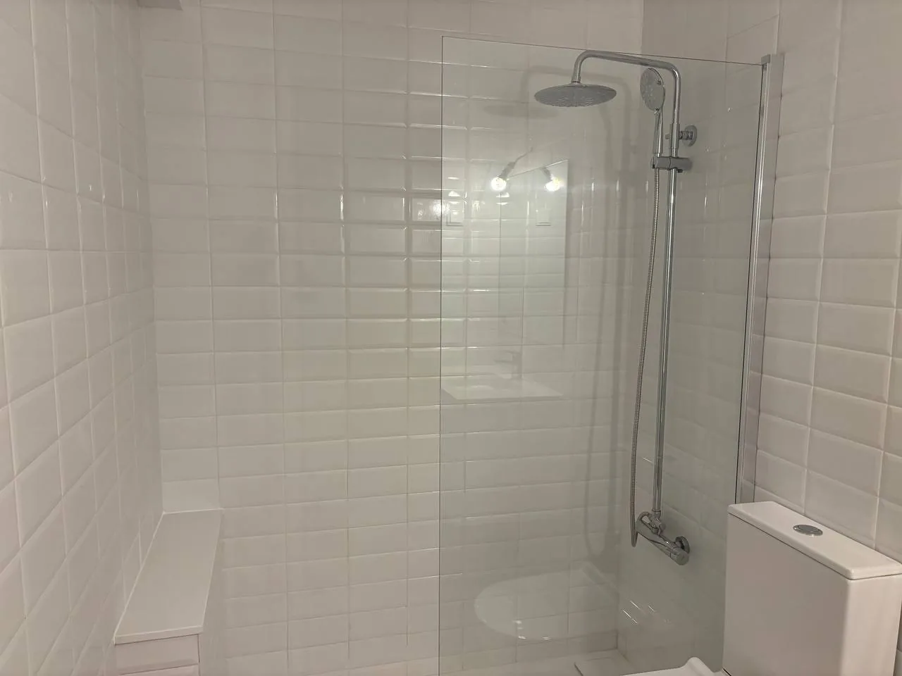 Shower area with white wall tiles and chrome fittings.