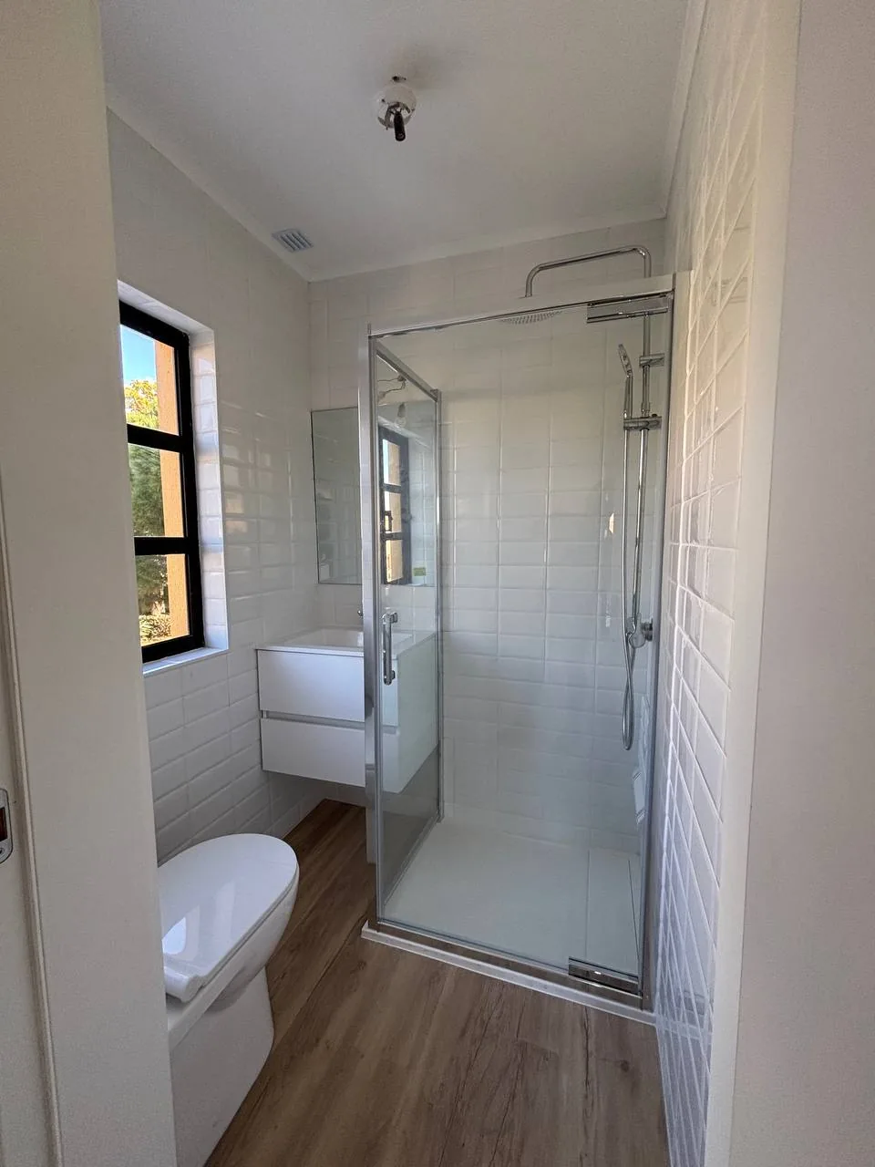 Tiled bathroom with a glass shower enclosure and a window on the left.
