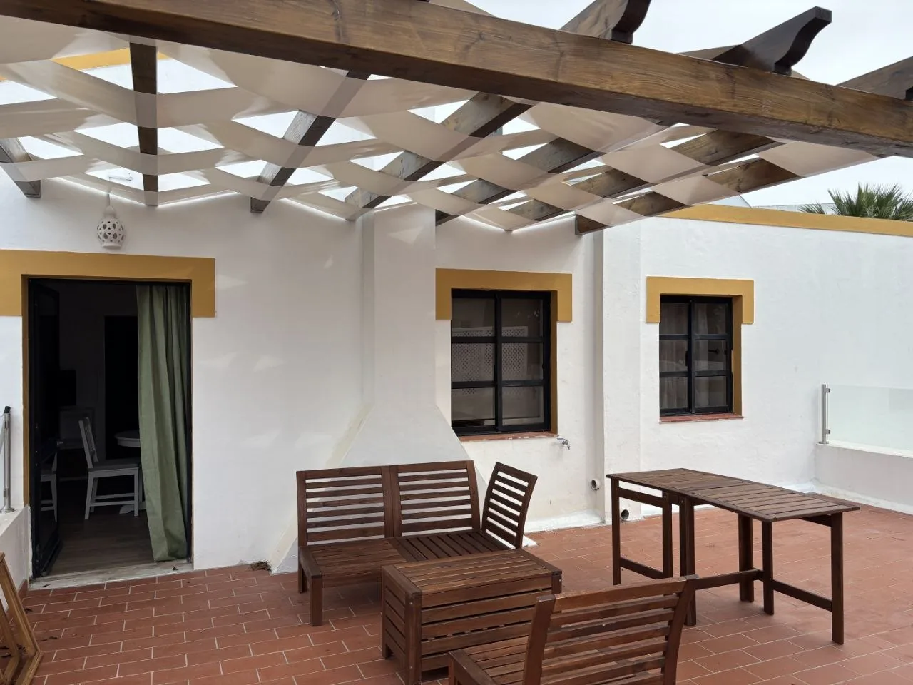 Terrace with a pergola, wooden seating and a doorway to the interior.